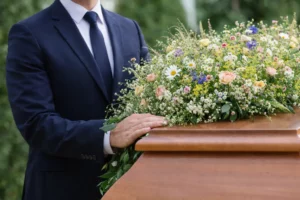 Main posée en hommage sur un cercueil en bois orné de fleurs champêtres